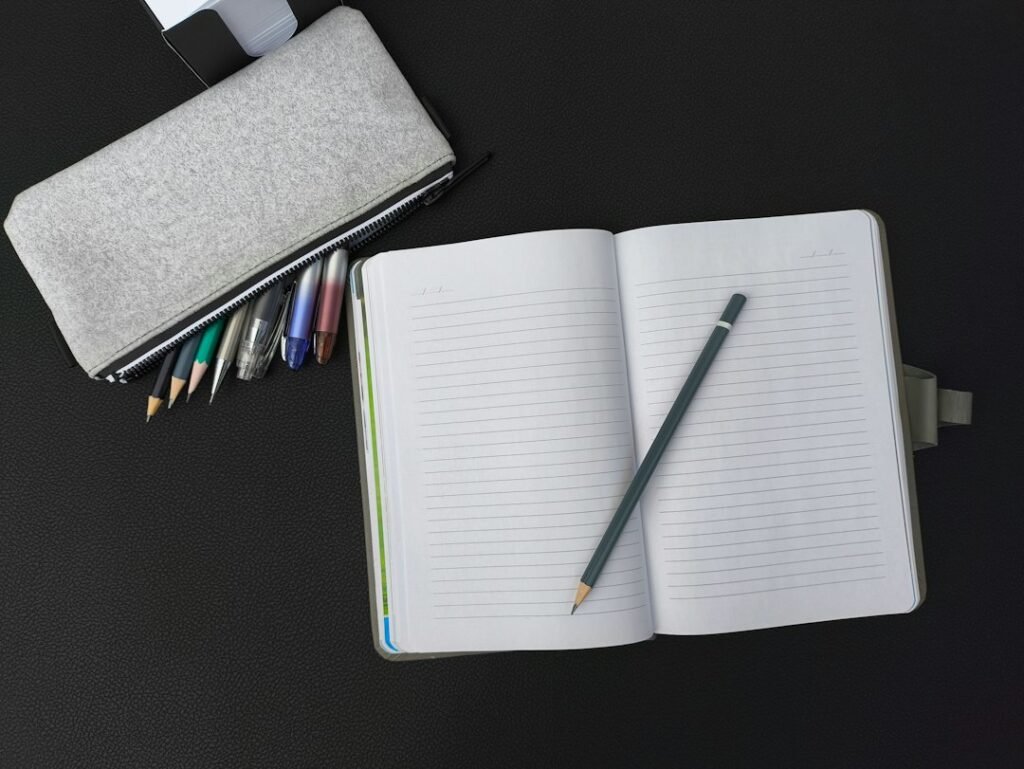 An open notebook with a pen and pencil on a table