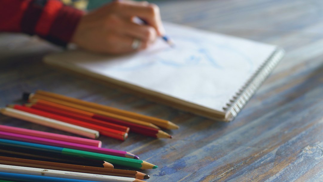 Artist sketching in notebook with colored pencils nearby