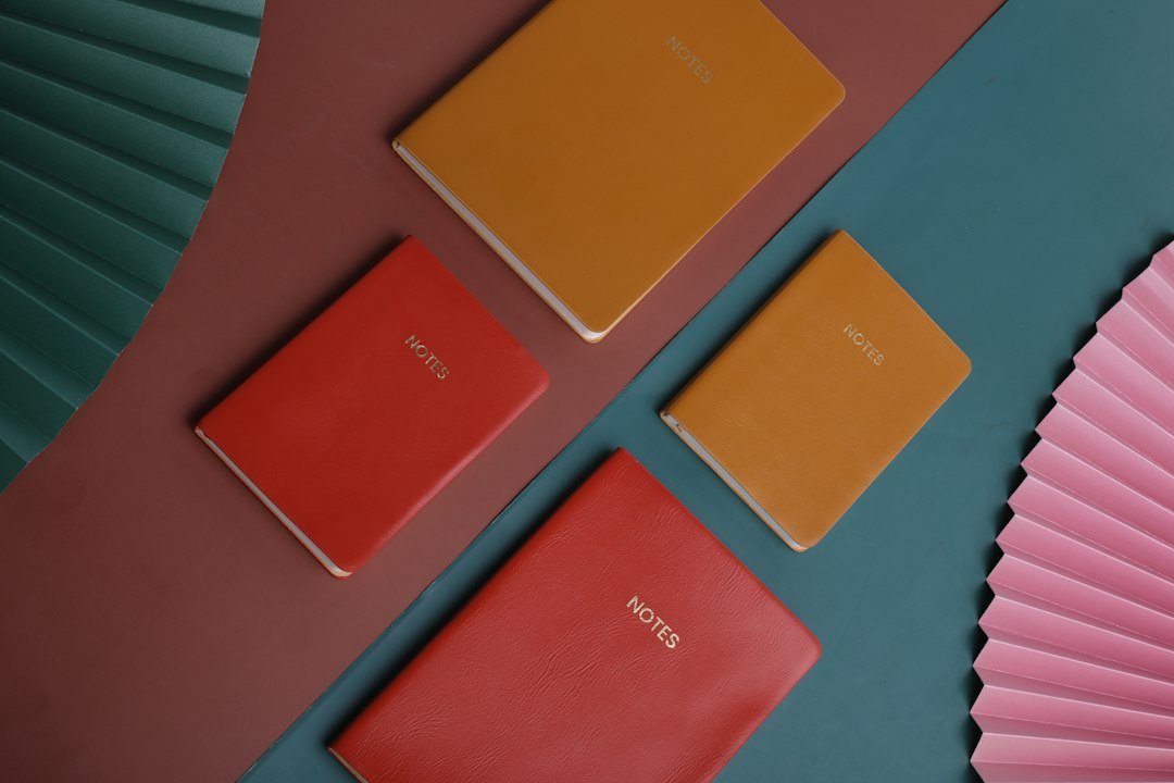 three different colored notebooks next to a pink fan